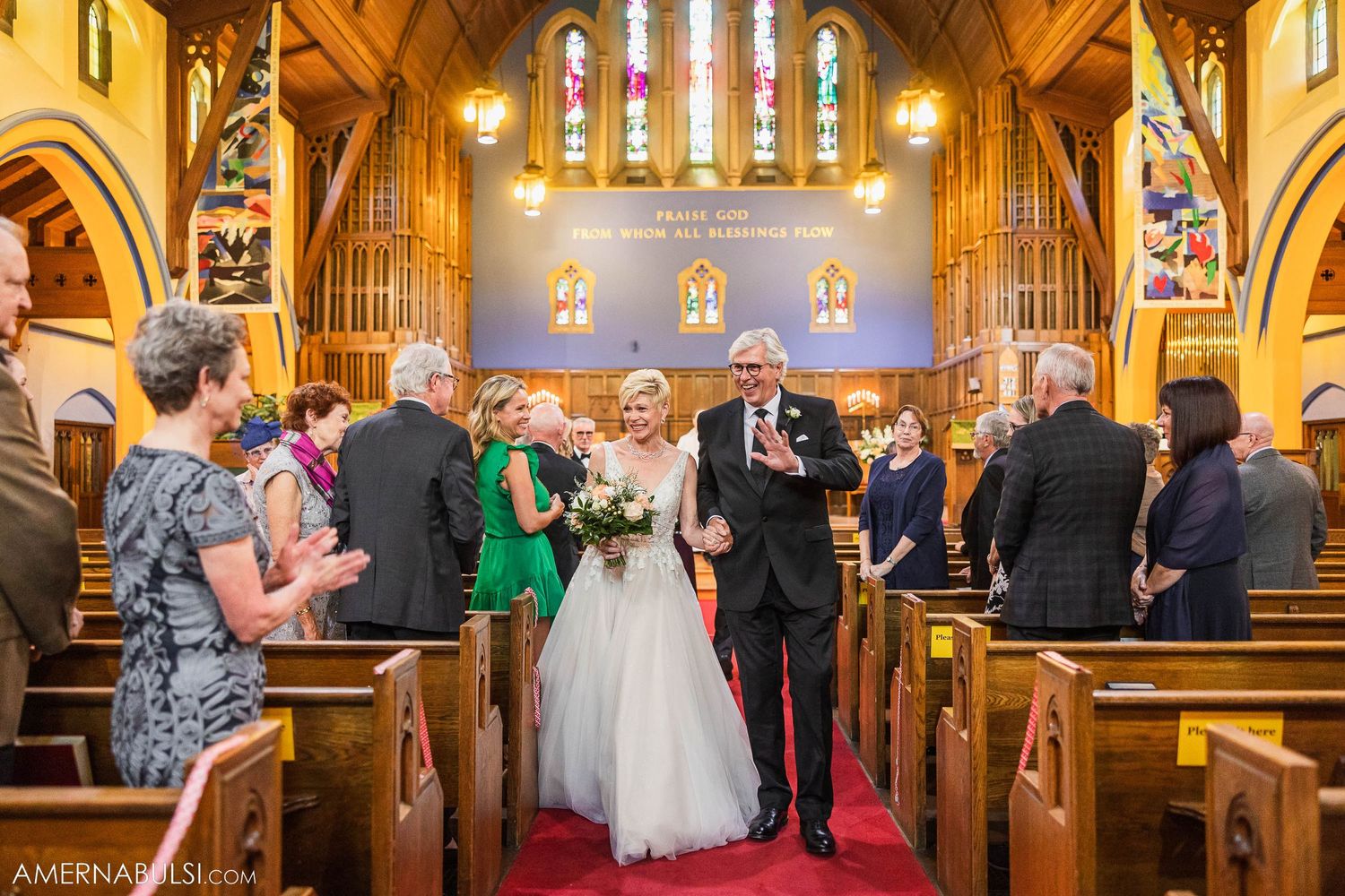 Newlyweds walking down church aisle while guests stand in celebration.