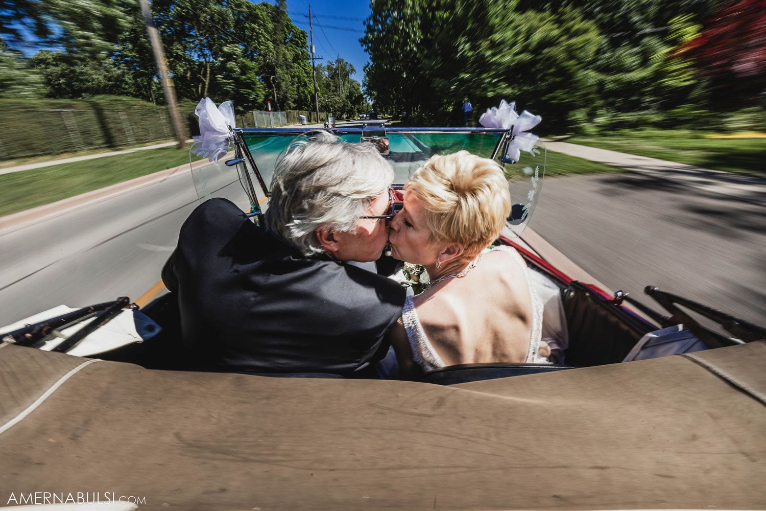 A couple sharing a romantic moment in the back seat of a moving vintage convertible.