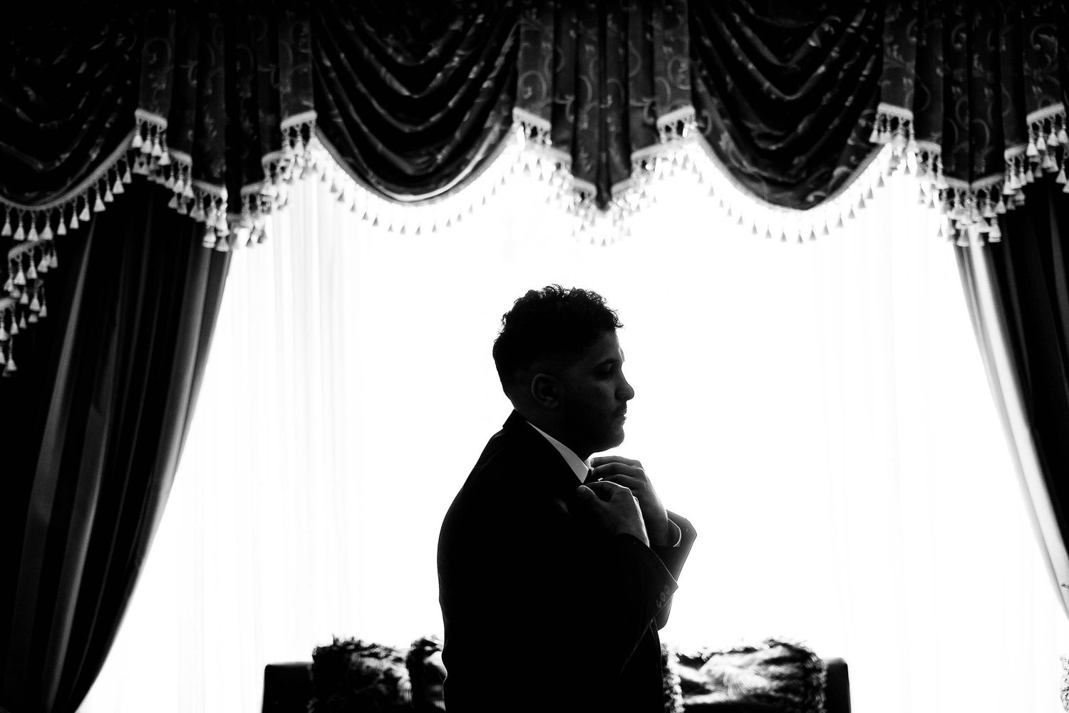 Dramatic black and white silhouette of a figure standing against ornate curtains.