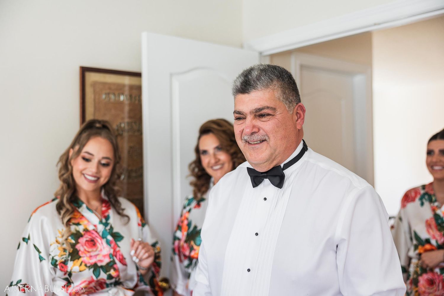 People in formal attire and floral robes share a joyful moment during wedding preparations.