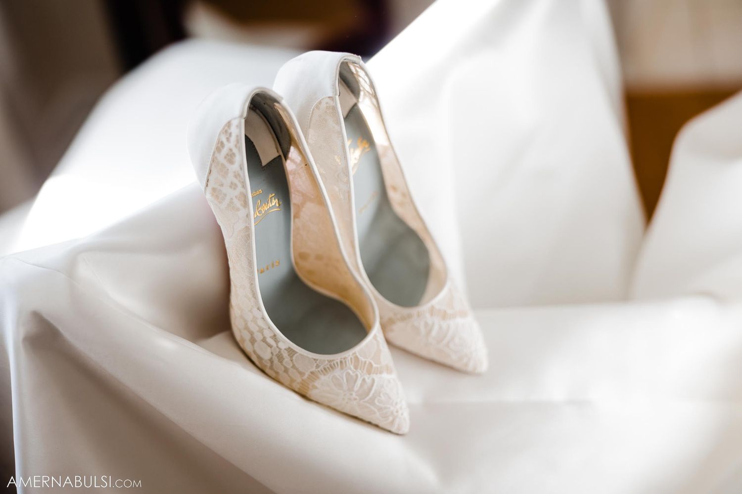 Elegant white lace bridal shoes displayed on white fabric.
