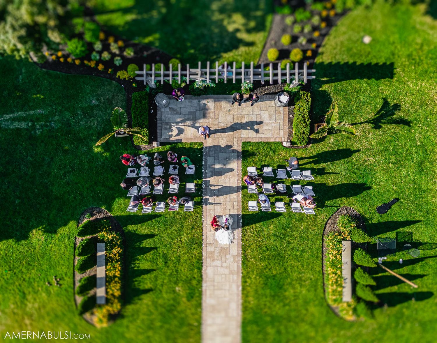 Aerial view of a wedding ceremony setup with white chairs arranged on a green lawn surrounded by trees.