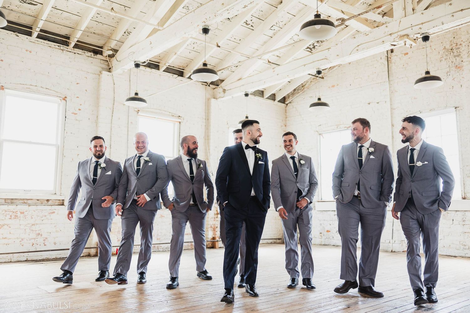 Groomsmen group photo with mixed grey suits surrounding central figure in black tuxedo.