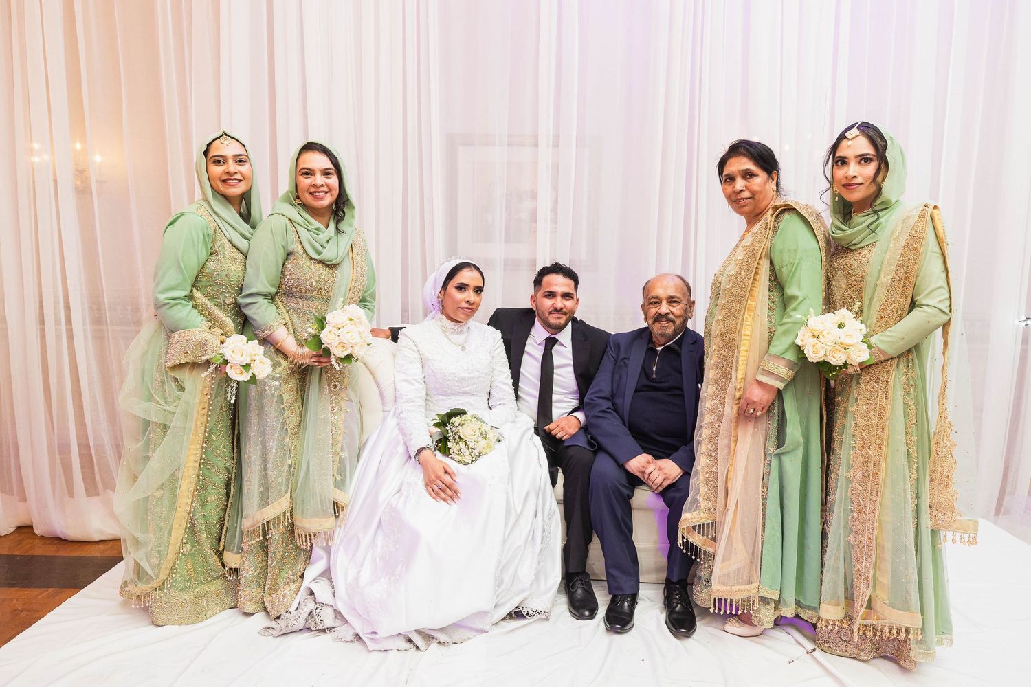 Wedding party in traditional attire poses for formal portrait against white backdrop.