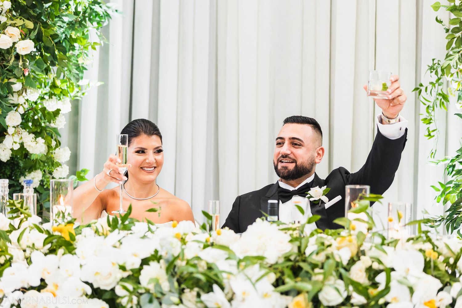 Wedding couple makes celebratory toast at elegant reception with floral decorations.