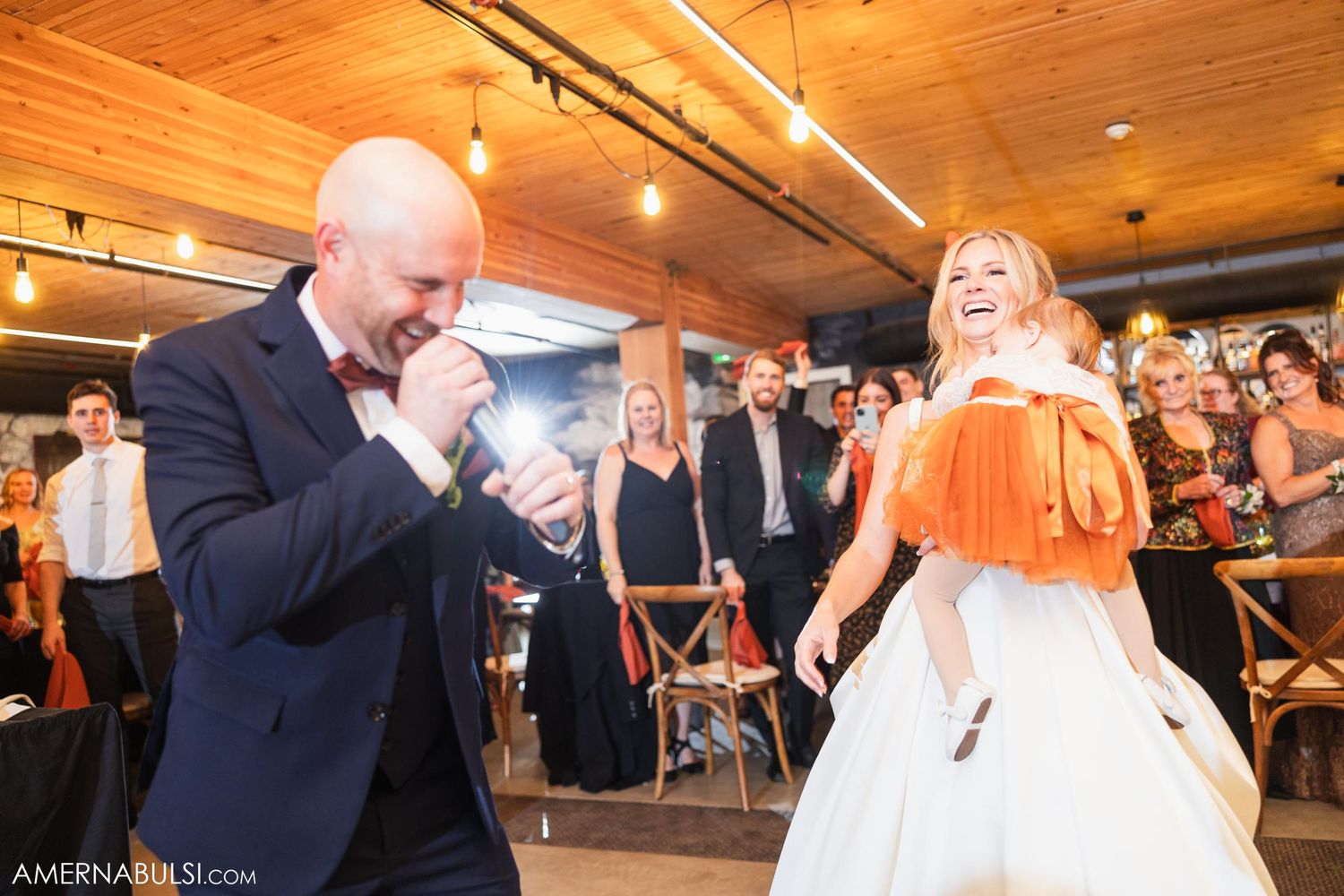 A couple shares a lively dance at their wedding reception under wooden beams and warm lighting.