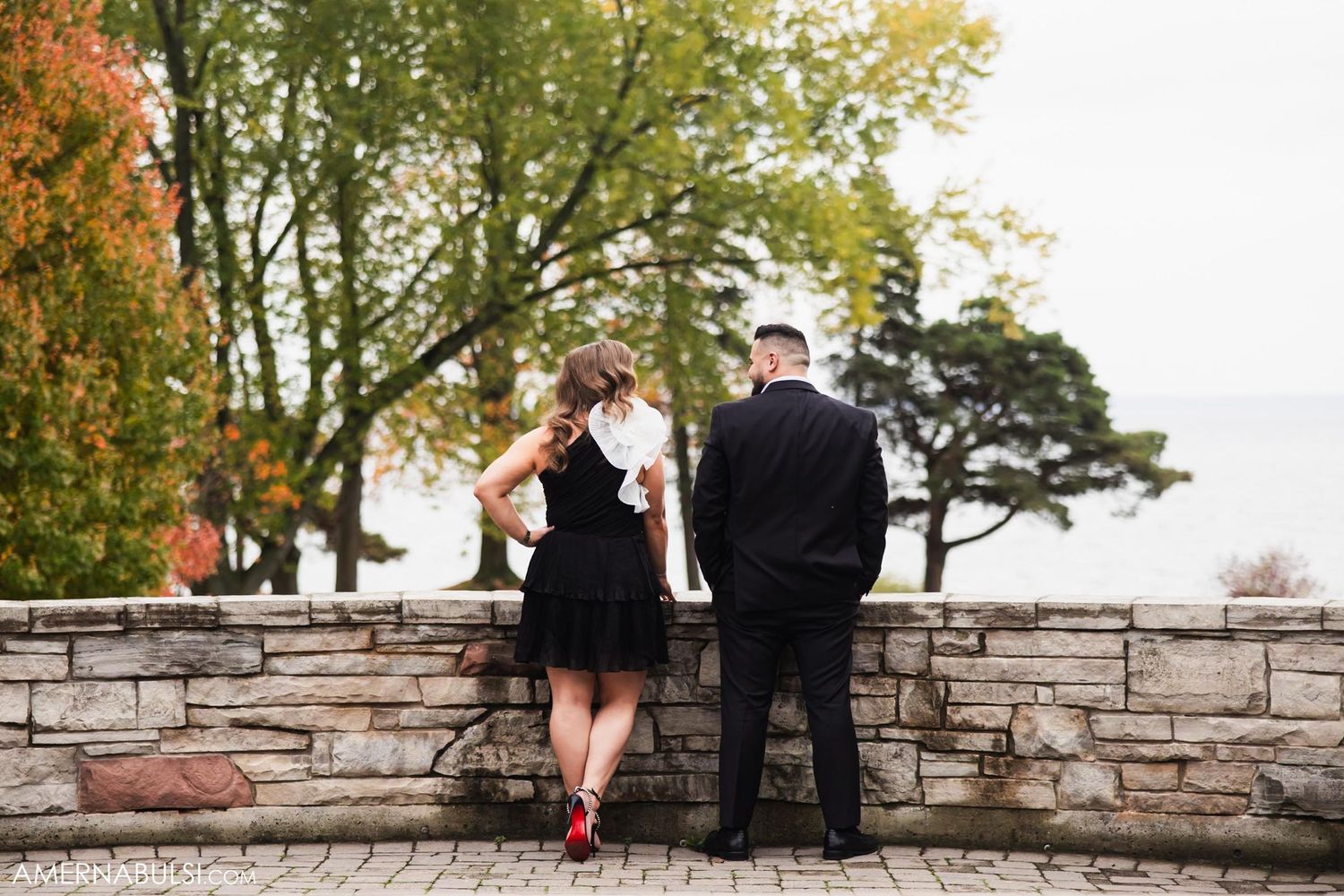 A couple stands against a stone wall during an autumn photoshoot.