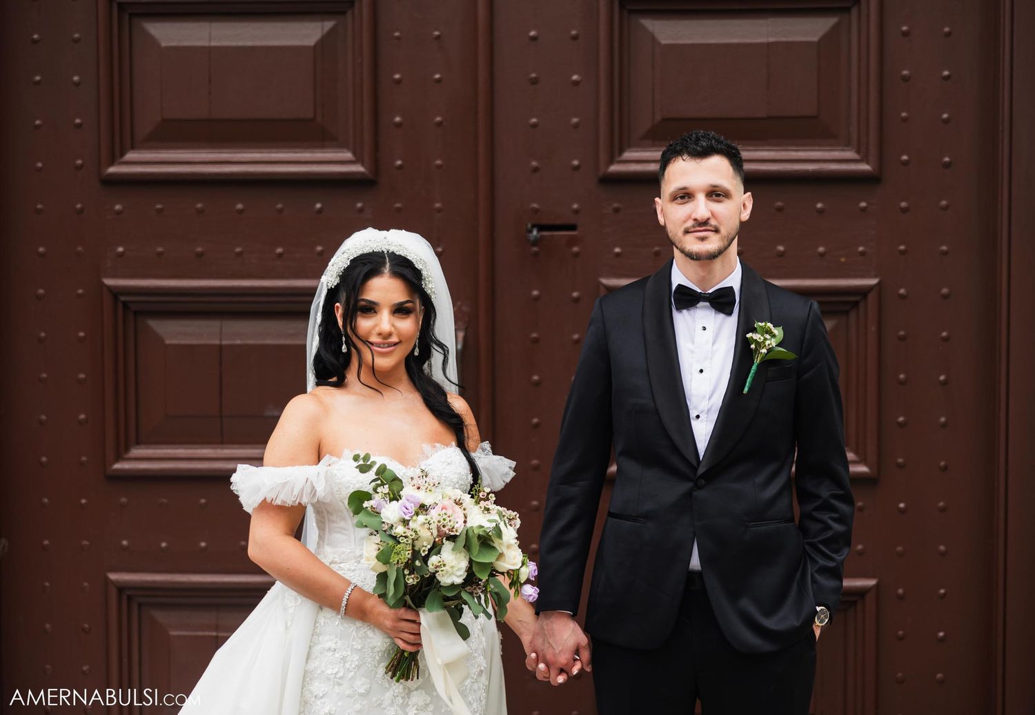 Classic wedding portrait in front of ornate brown wooden doors.