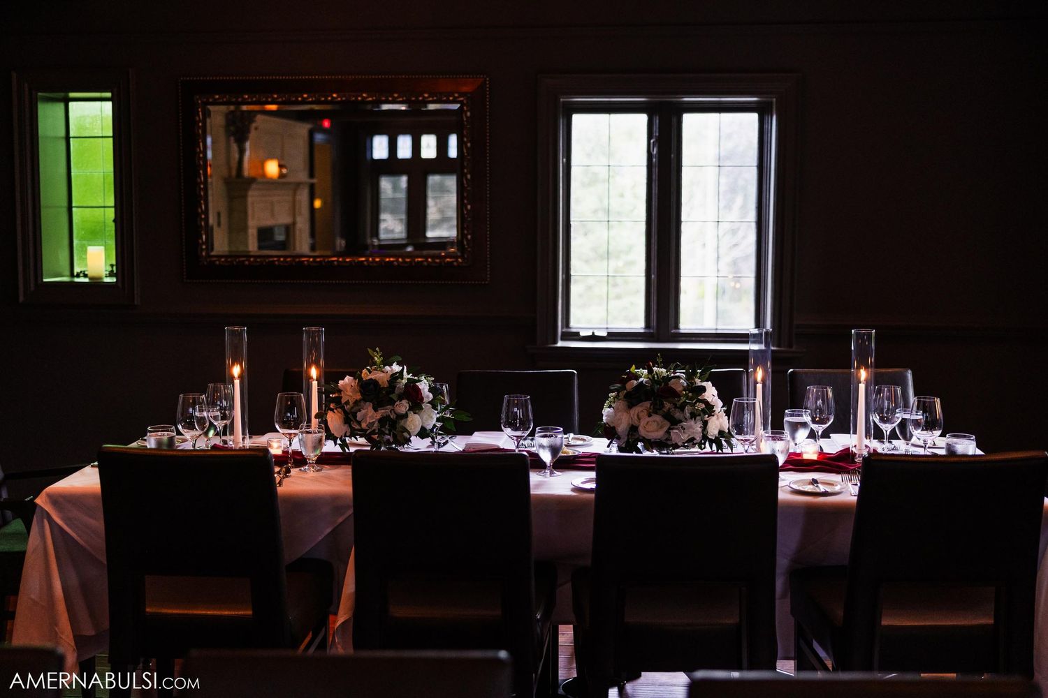Moody dining room with elegant table settings lit by candlelight and natural window light.