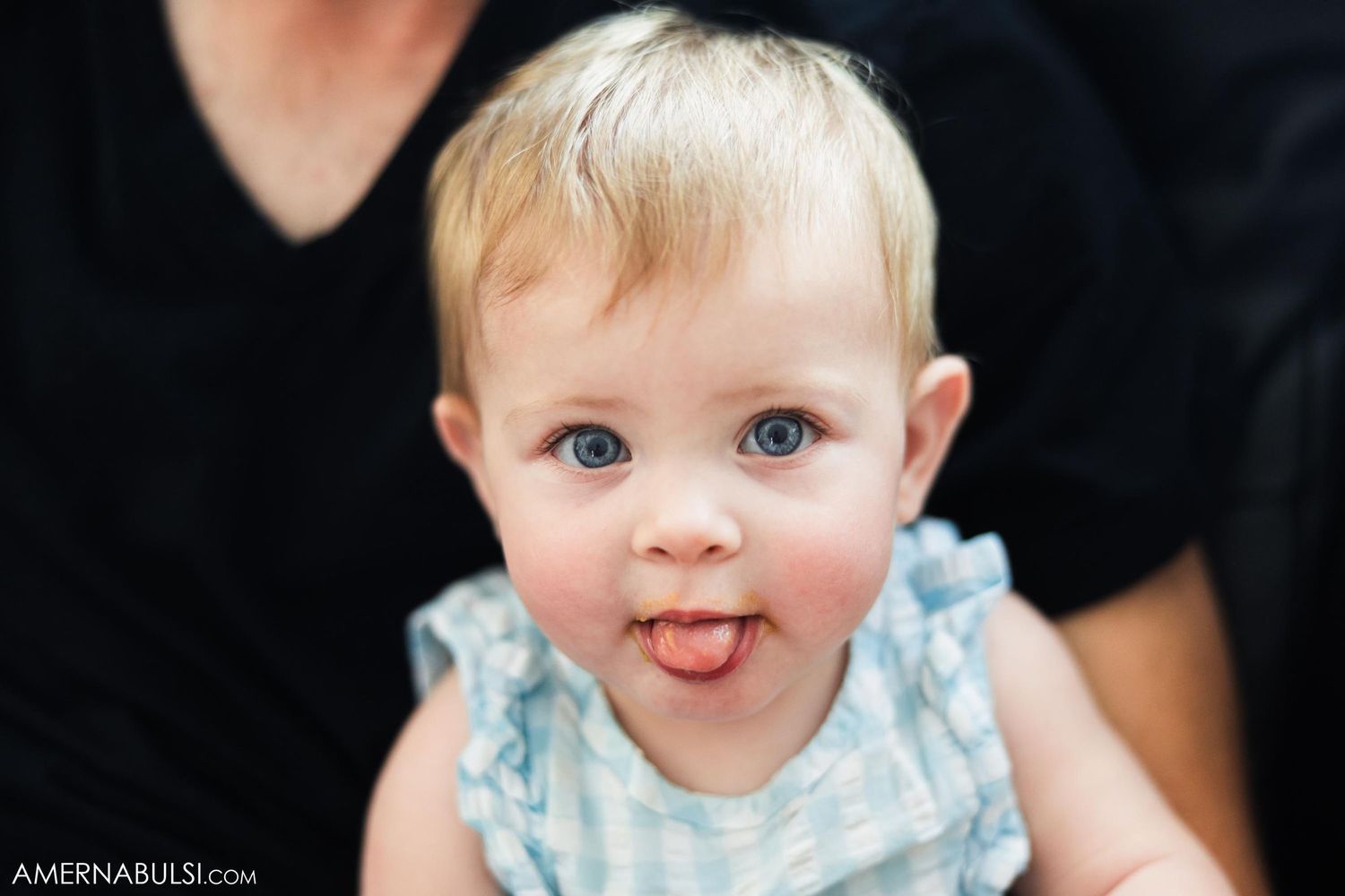 A young child in light blue clothing sticking their tongue out playfully at the camera.