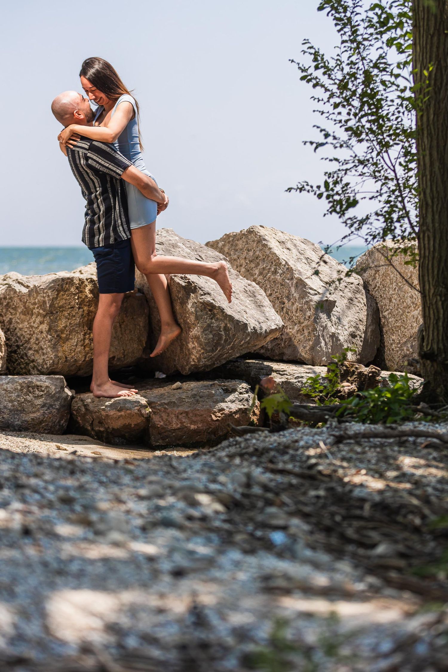 Romantic couple embracing on rocky beach shoreline during summer.
