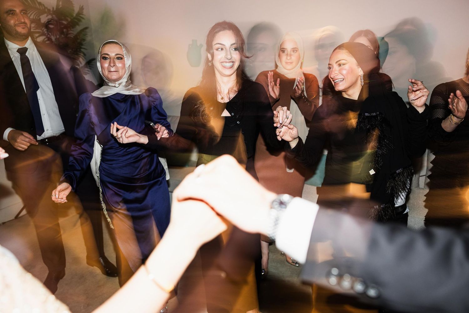 Wedding guests dance and celebrate together at an indoor reception venue with atmospheric lighting.