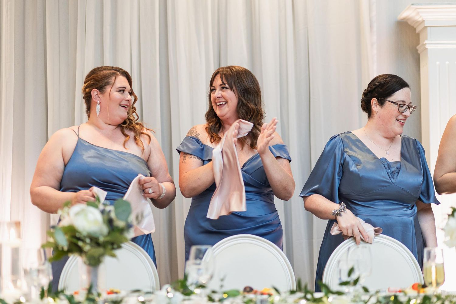 Bridesmaids in blue dresses laughing and having fun at wedding reception.