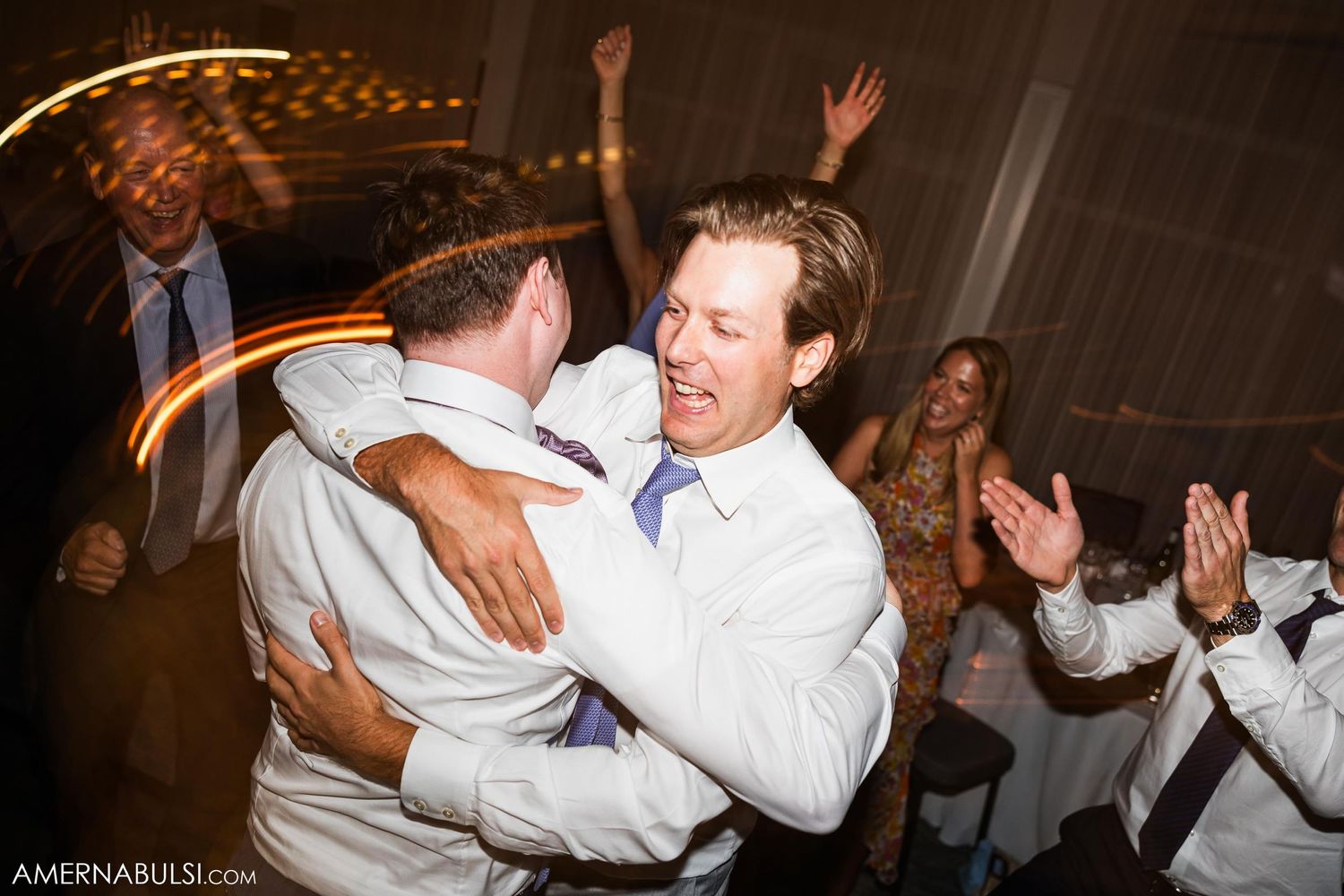 Guests celebrate joyfully on the dance floor at an indoor wedding reception.
