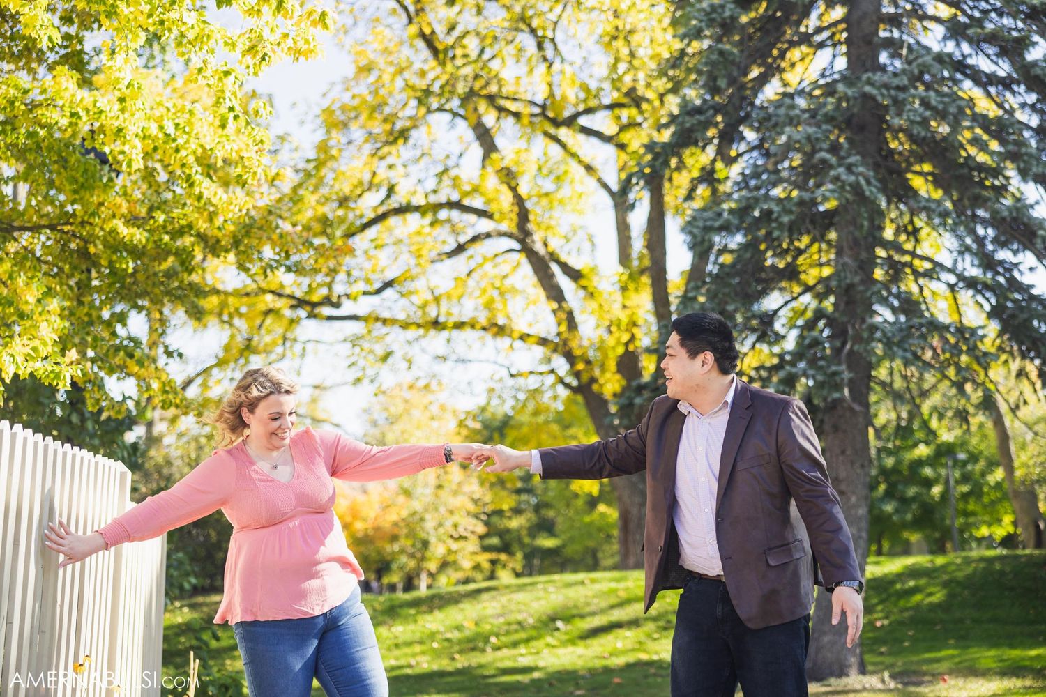 Couple playing and holding hands in sunlit garden with fall foliage.