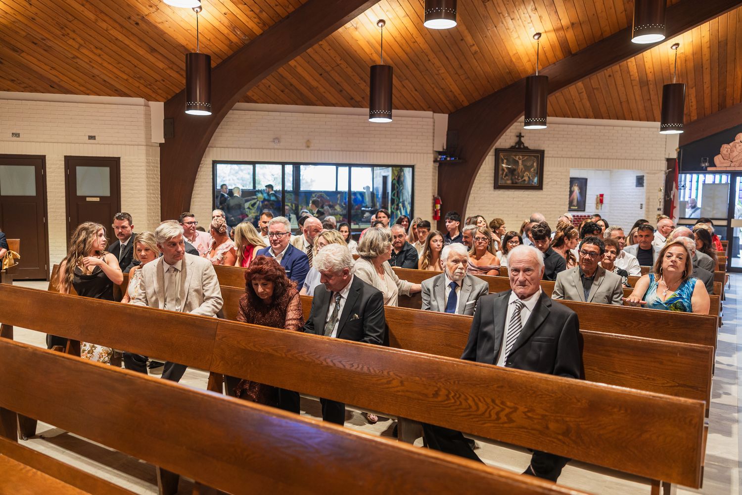 Guests seated in wooden church pews during a wedding ceremony in a modern chapel.