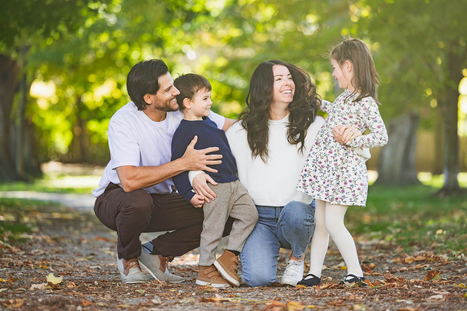 Family sitting together on autumn leaves in a park during a golden sunset photo session.