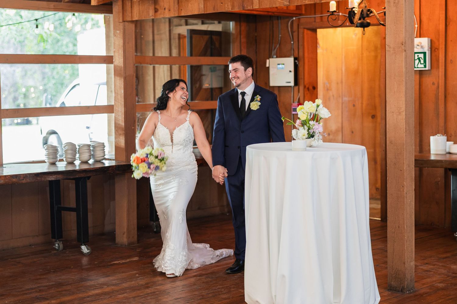 Bride and groom hold hands smiling as they enter their rustic wooden wedding reception venue.