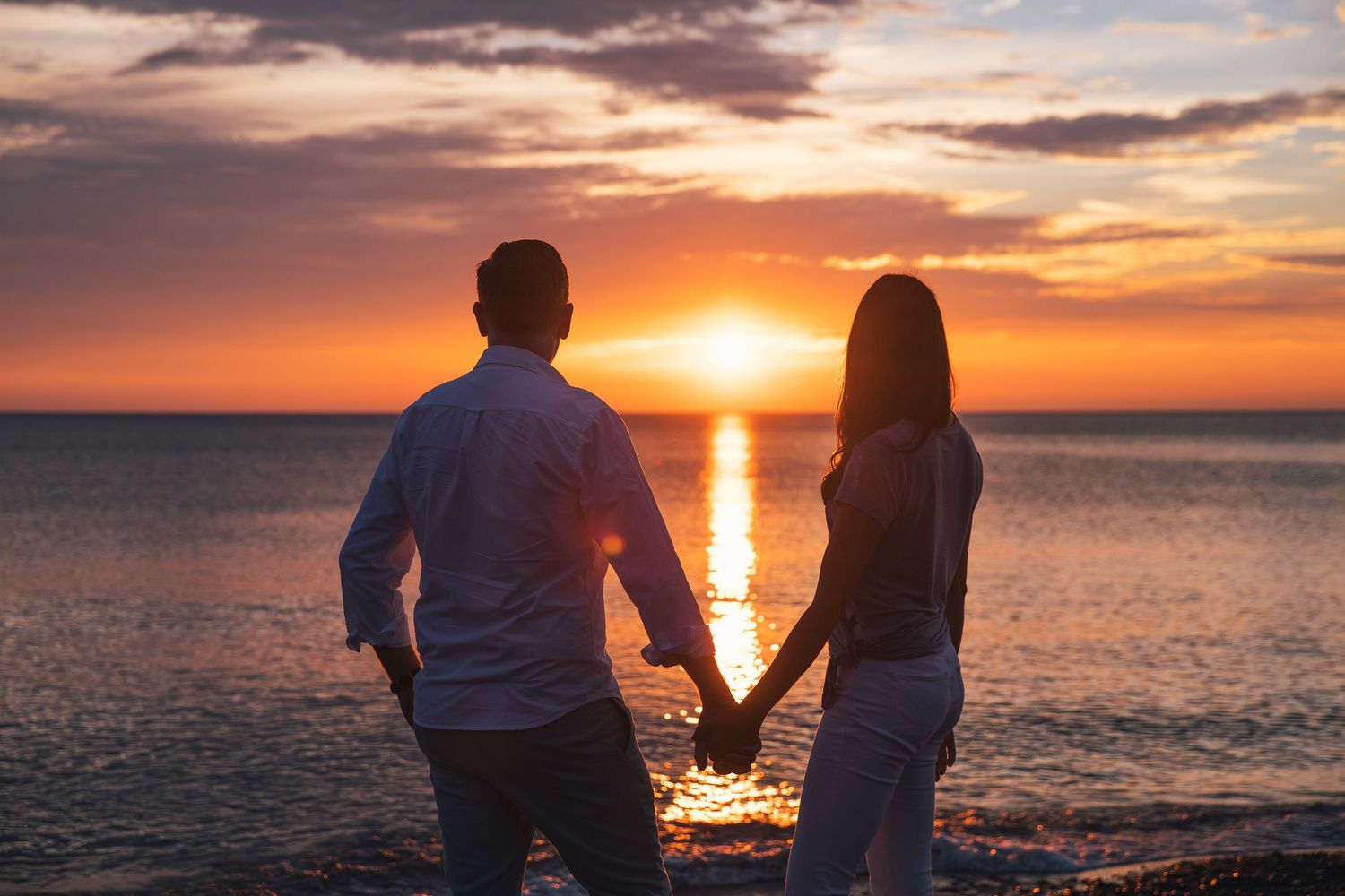 Silhouettes against vibrant orange sunset over calm ocean waters.
