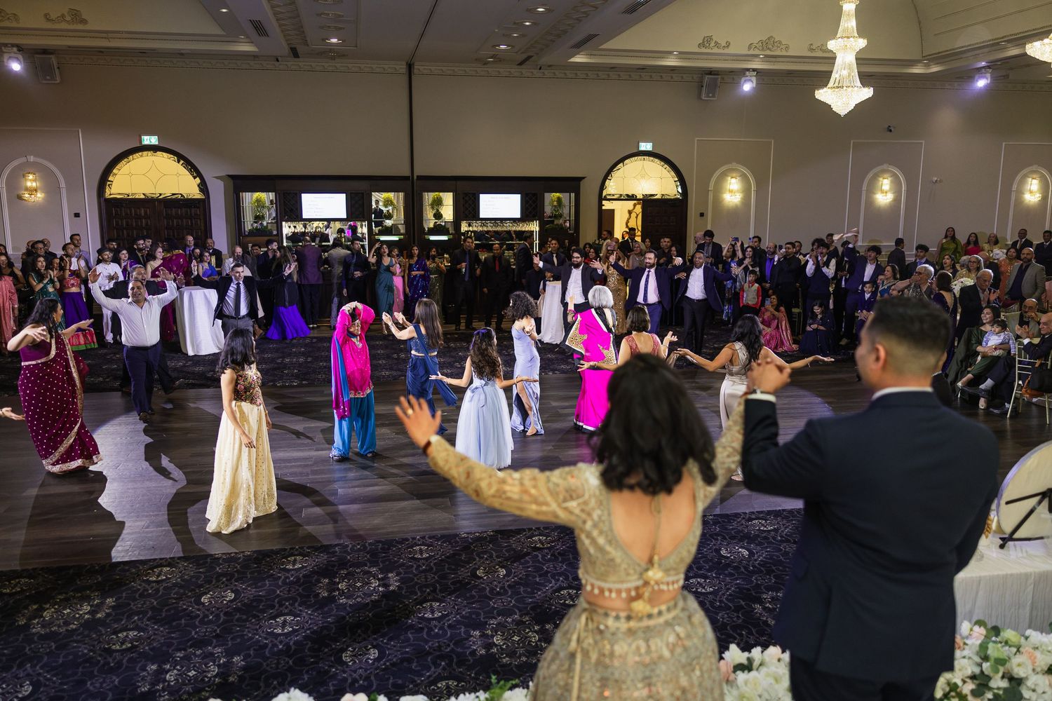 Panoramic view of a formal ballroom event with dancers and spectators under elegant chandeliers.