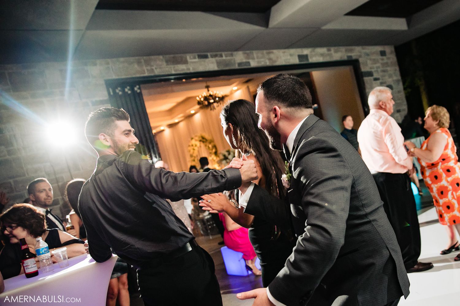 Wedding reception dance floor filled with guests celebrating under dramatic lighting.