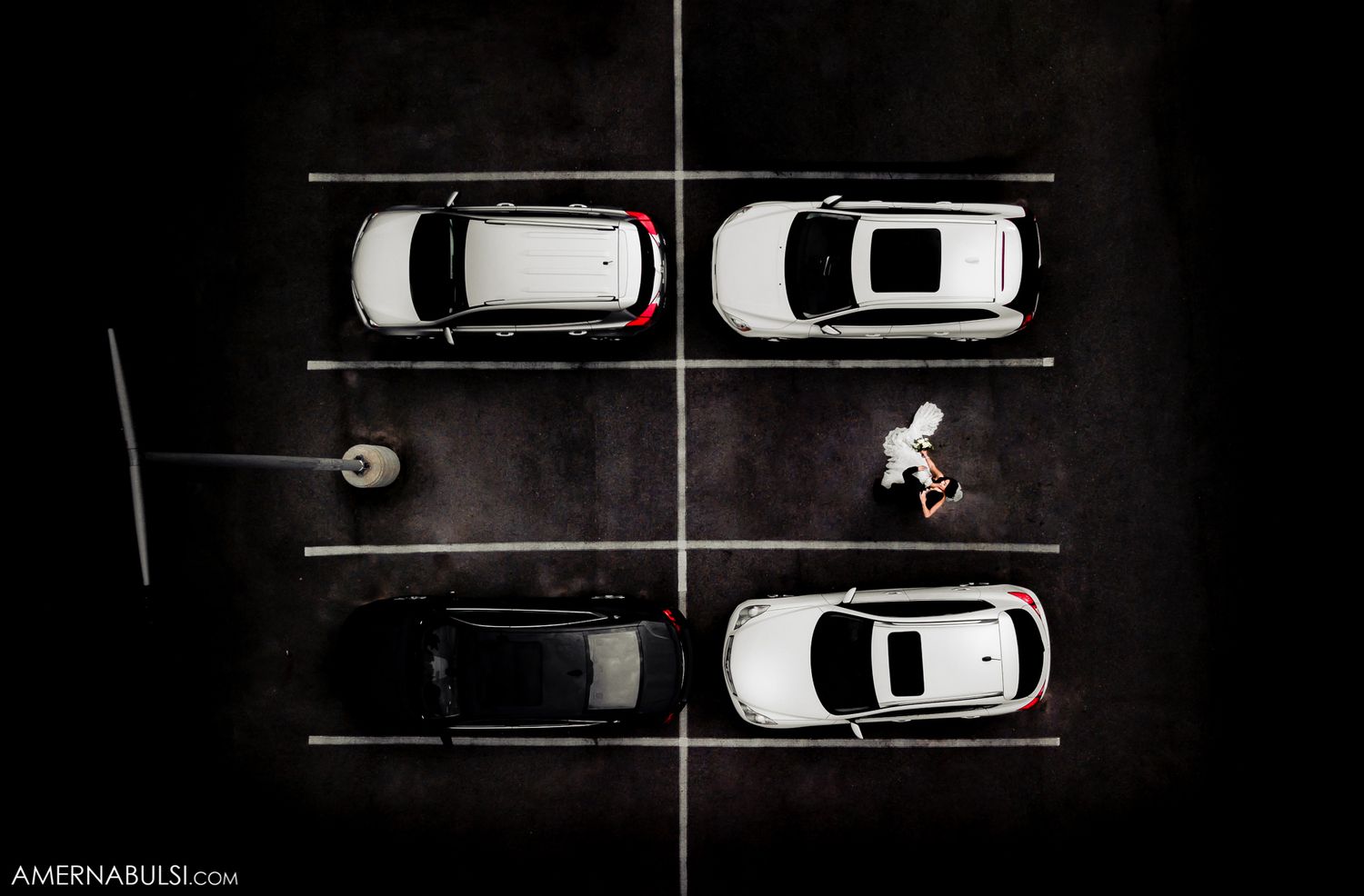 Aerial view of parked cars and lone cyclist in parking lot at night.