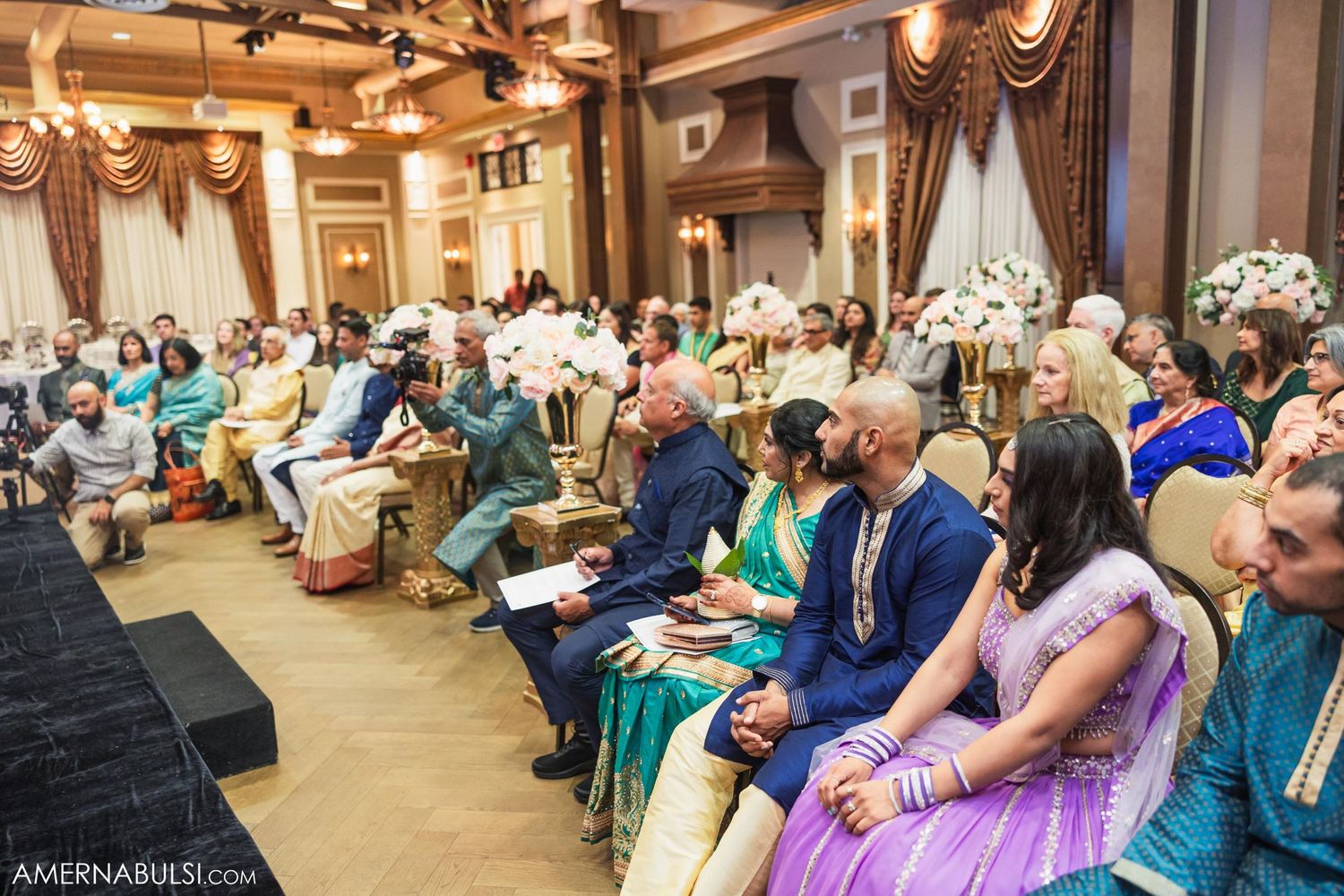 Wedding guests in colorful traditional Indian attire seated in rows during a formal ceremony.