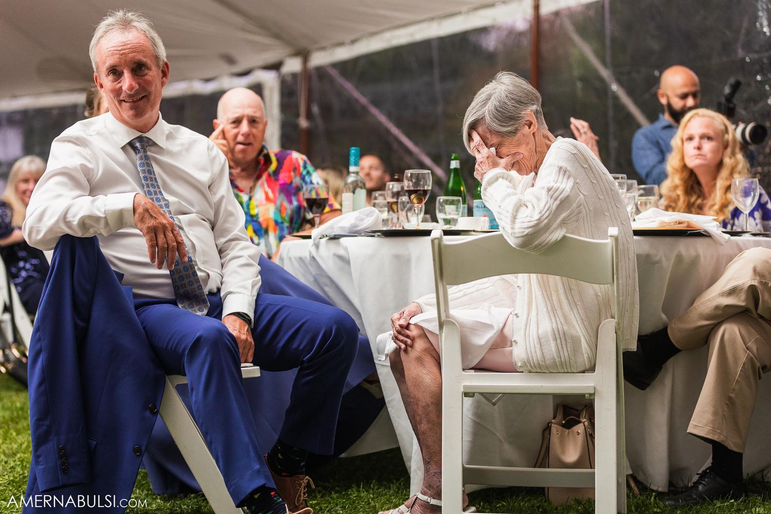 Wedding guests relax at outdoor reception tables under a white tent.