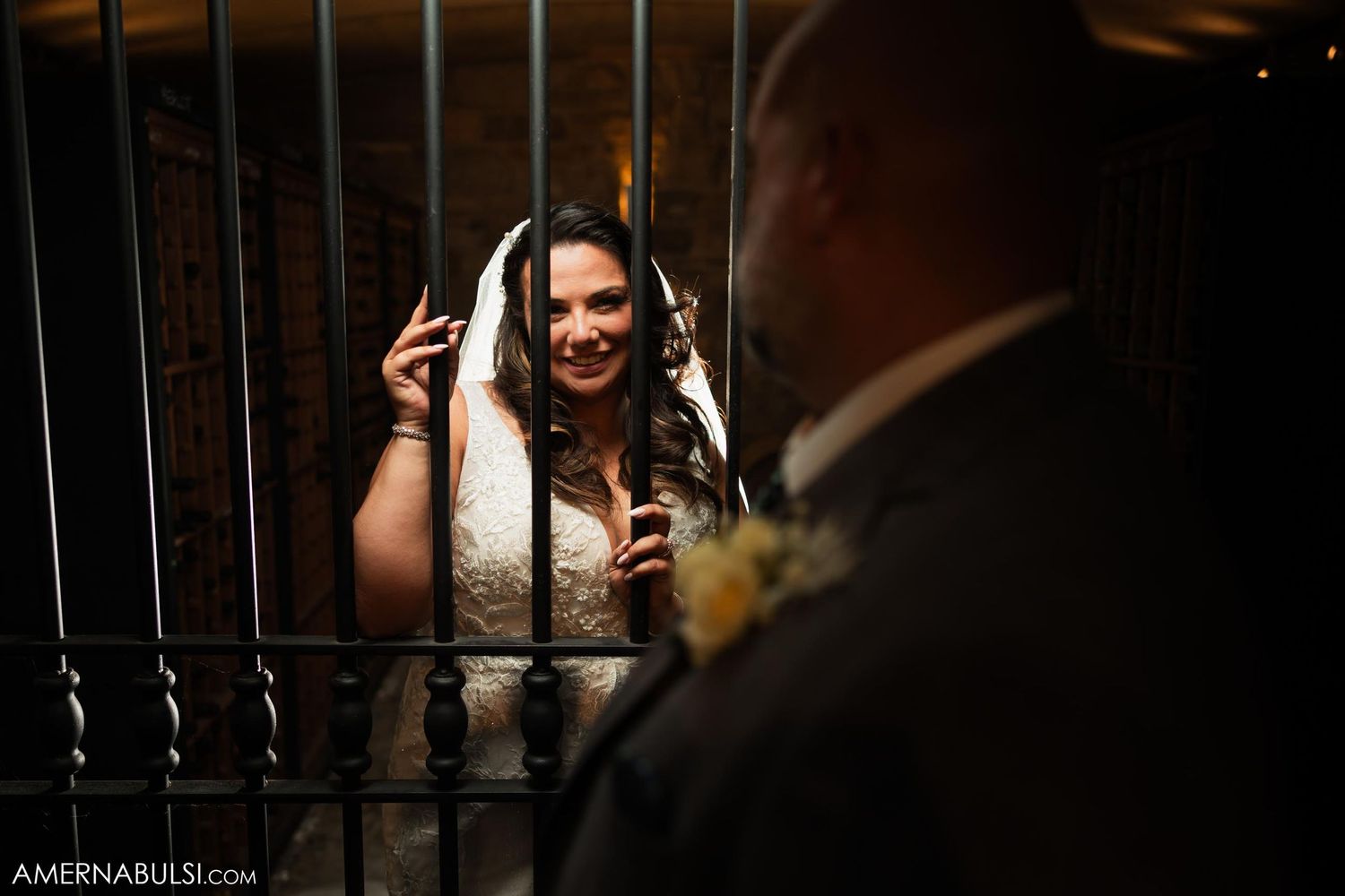 Bride smiling through decorative bars while interacting with someone during wedding celebration.