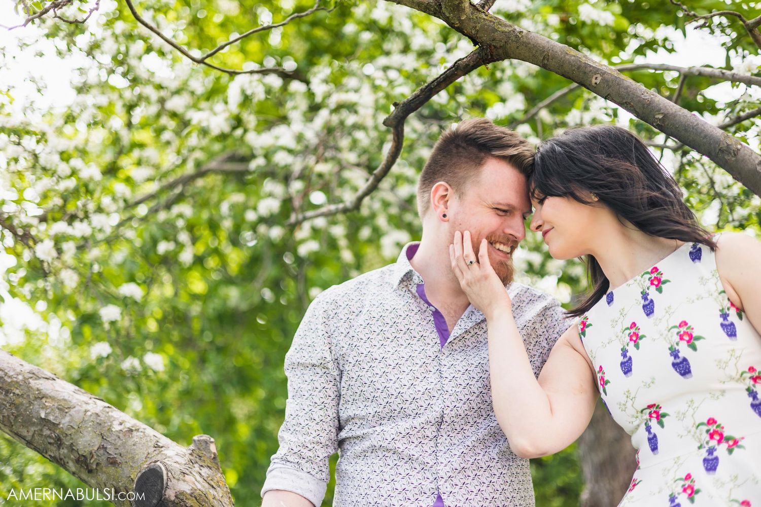 A tender moment shared between a couple beneath green spring foliage.