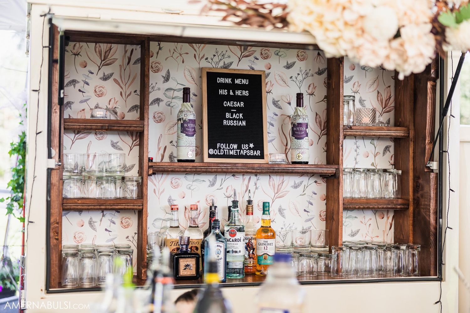 Rustic wooden bar display with glasses and liquor bottles at wedding reception.