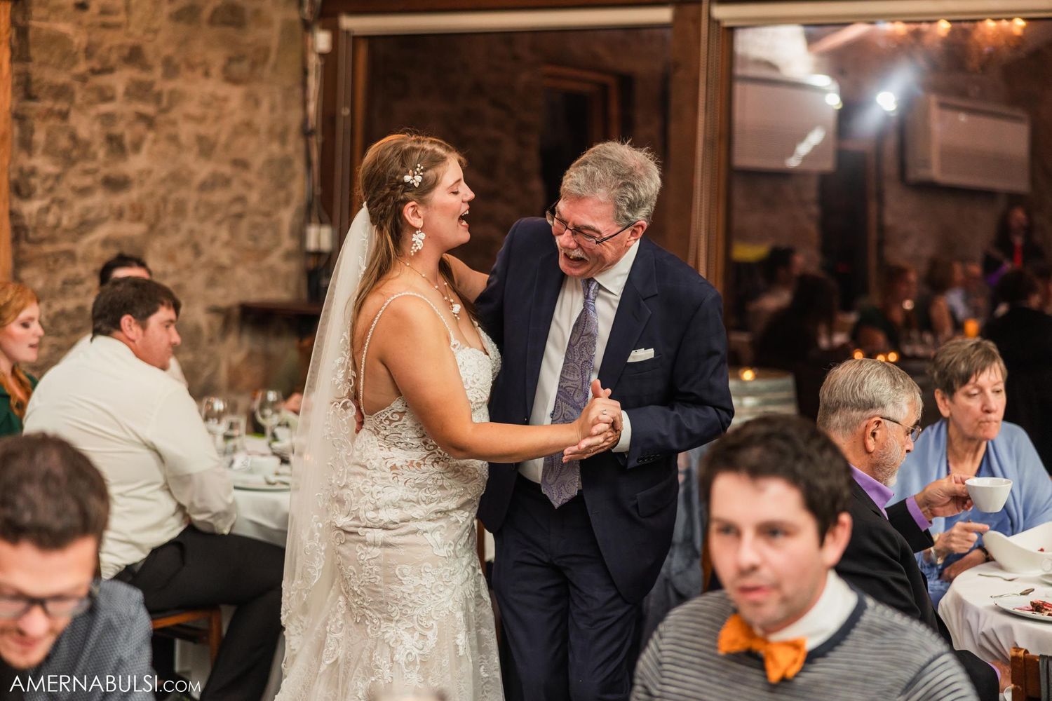 Couple sharing intimate dance moment in rustic reception venue with stone walls and chandeliers.