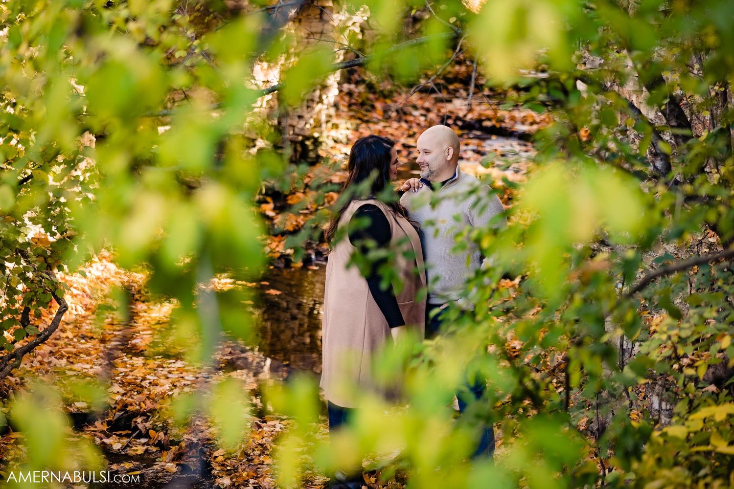 Romantic portrait through green foliage with stone ruins and autumn colors in background.