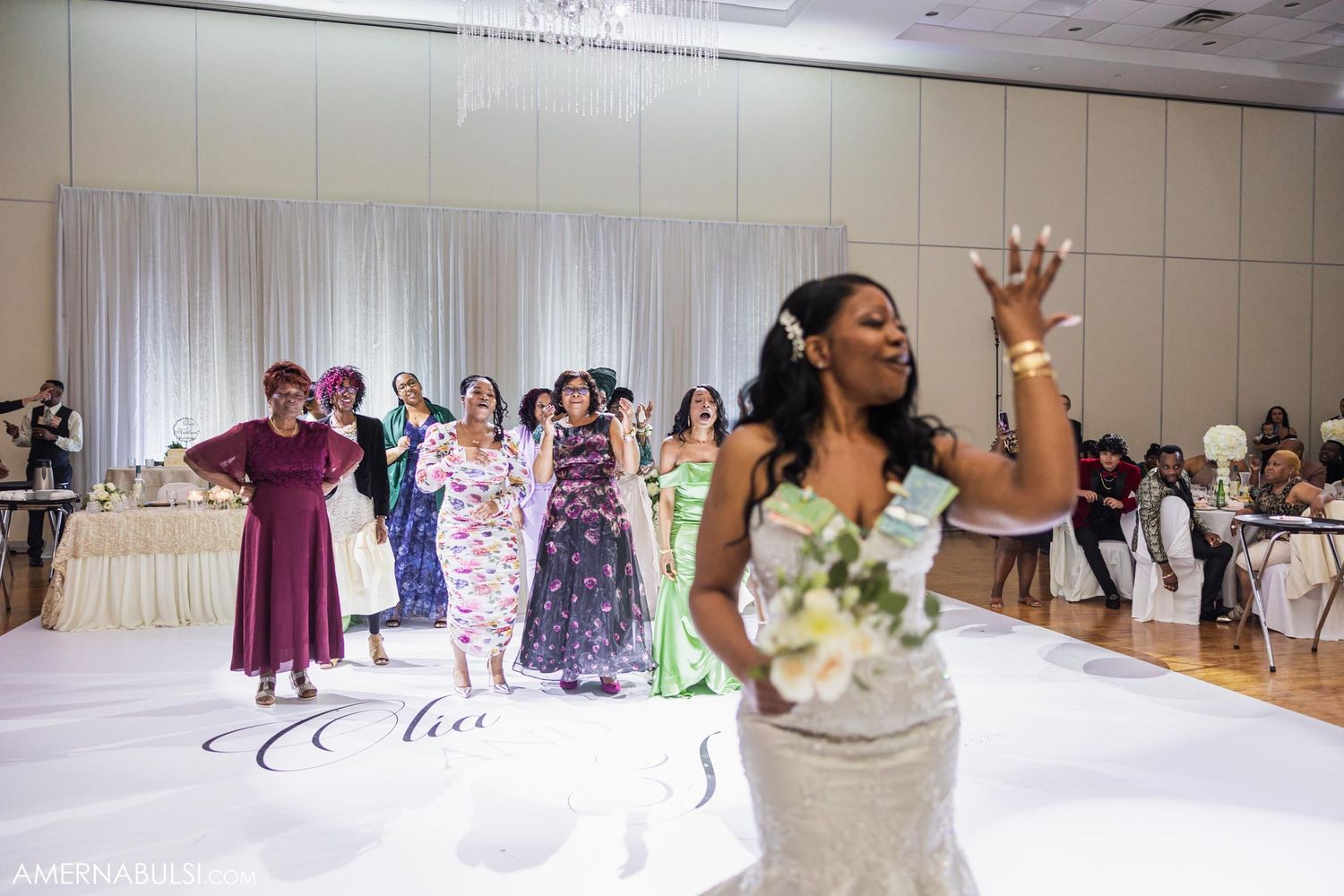 Bride tosses her bouquet during reception while wedding guests in colorful dresses look on.