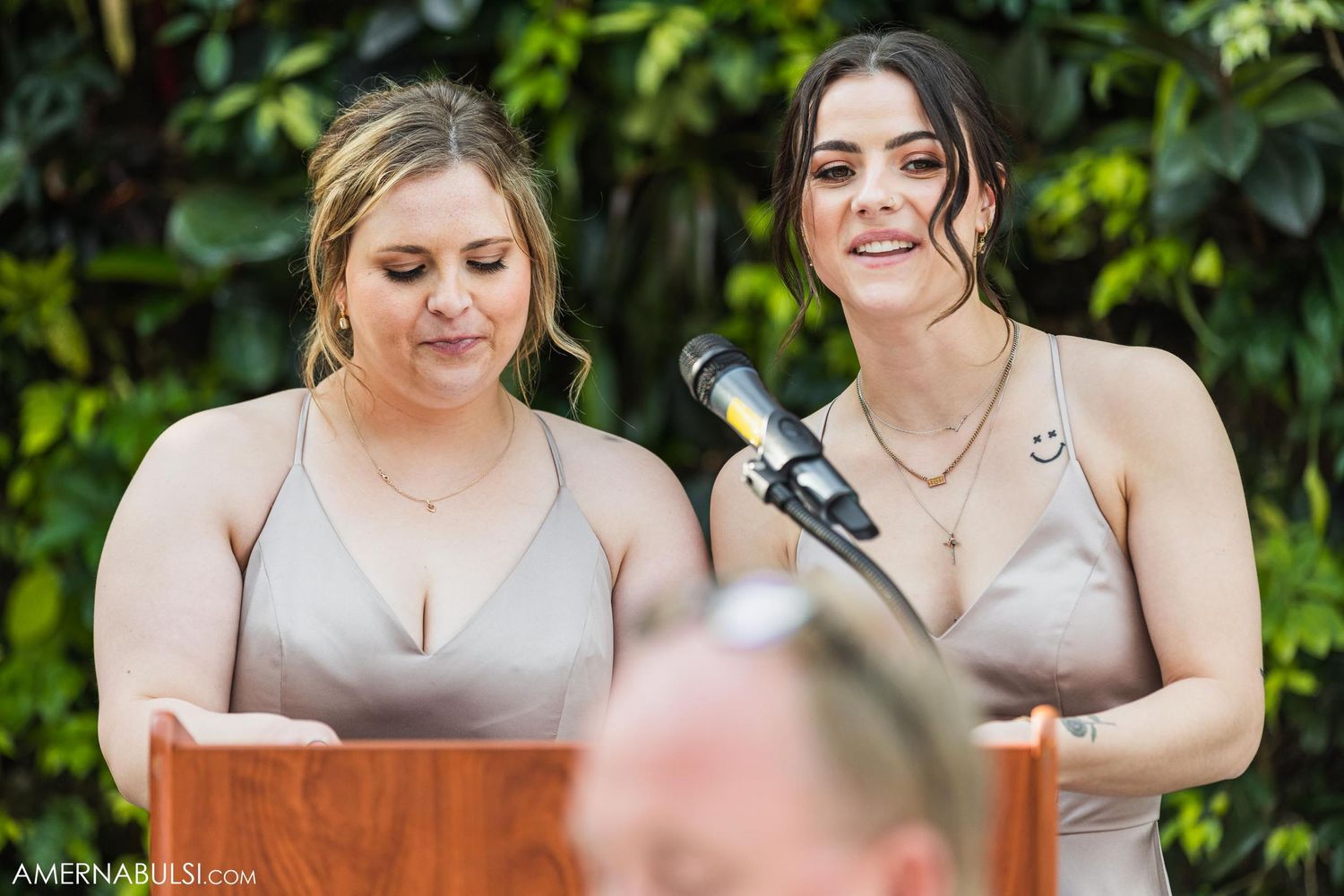 Two people in light-colored formal dresses giving speeches at a podium during a wedding ceremony.