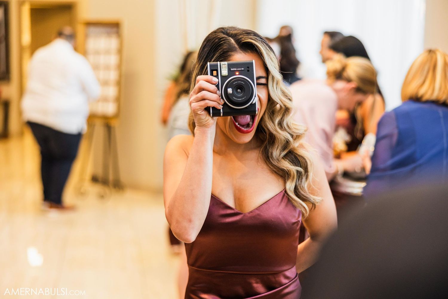 Wedding guest in burgundy dress capturing photos with vintage-style camera.