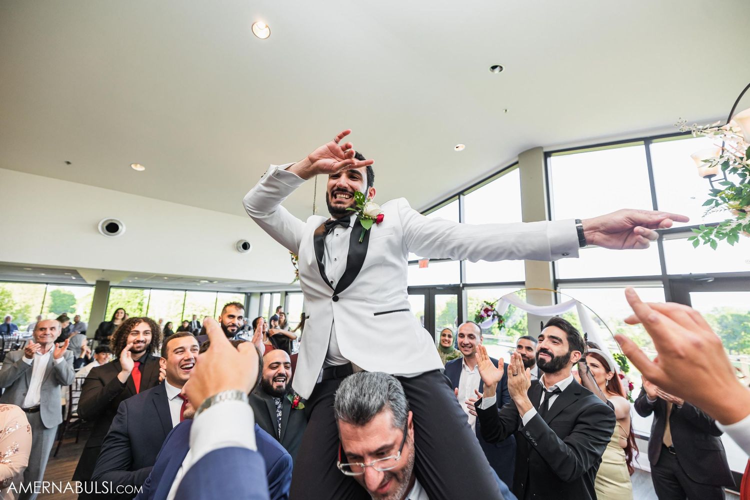 Groom being lifted up and celebrated by enthusiastic wedding guests during reception festivities.