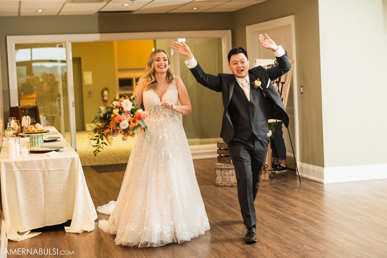 Bride in lace gown and groom make joyful entrance at wedding reception.