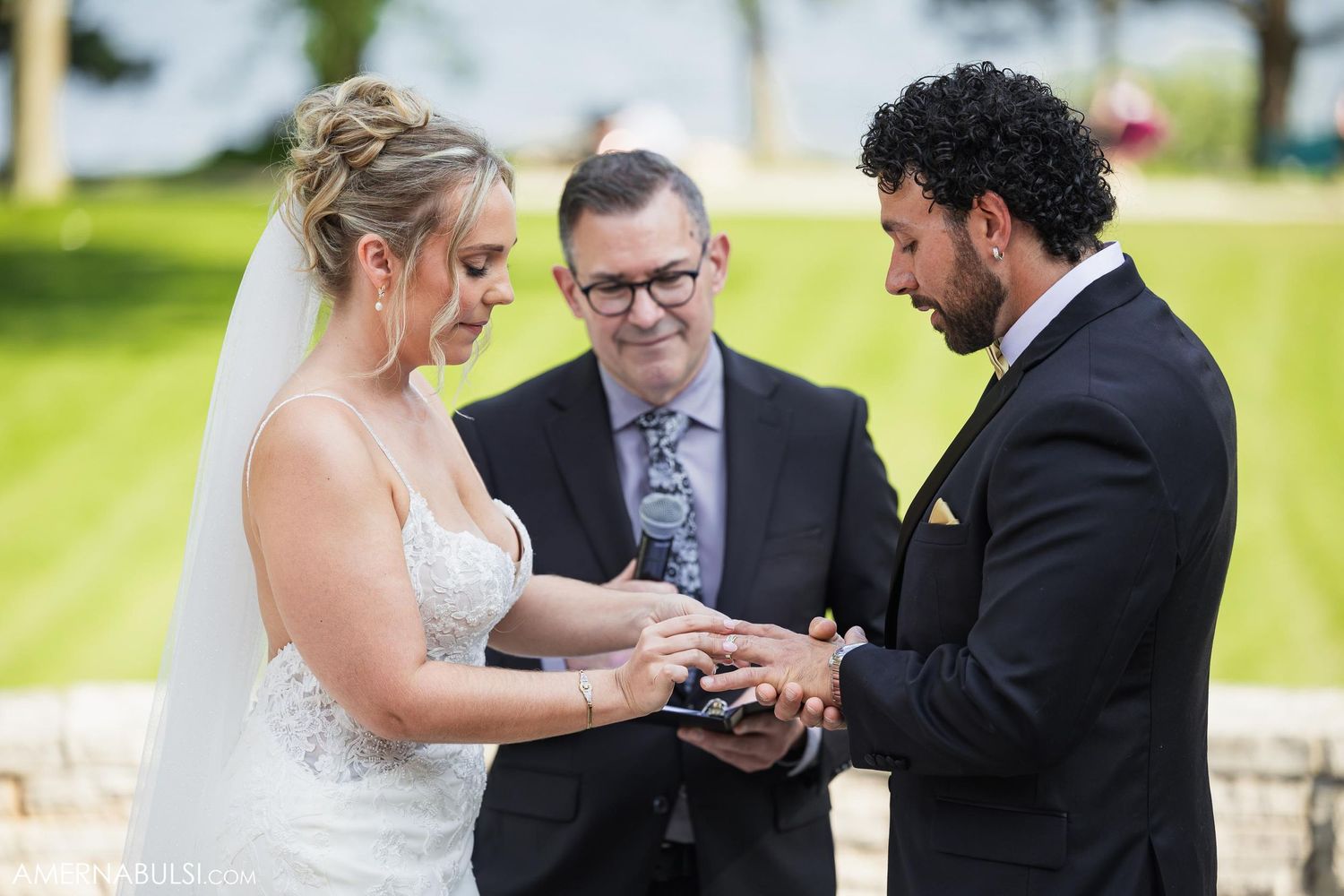 Wedding ceremony showing exchange of rings on stone terrace with water views in background.