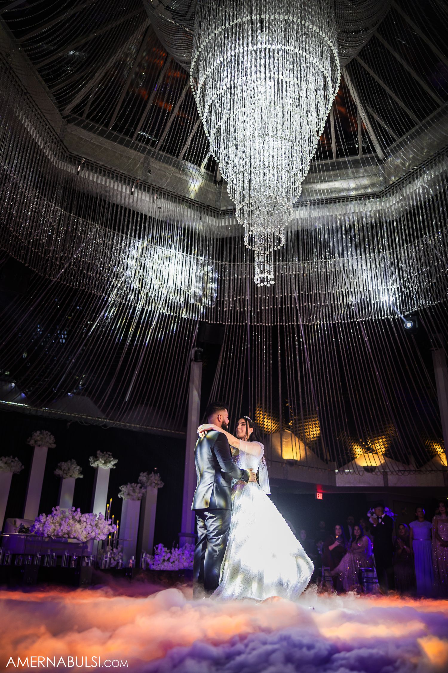 Elegant wedding dance scene with fog effects and crystal chandeliers creating a dreamy atmosphere in a grand ballroom.