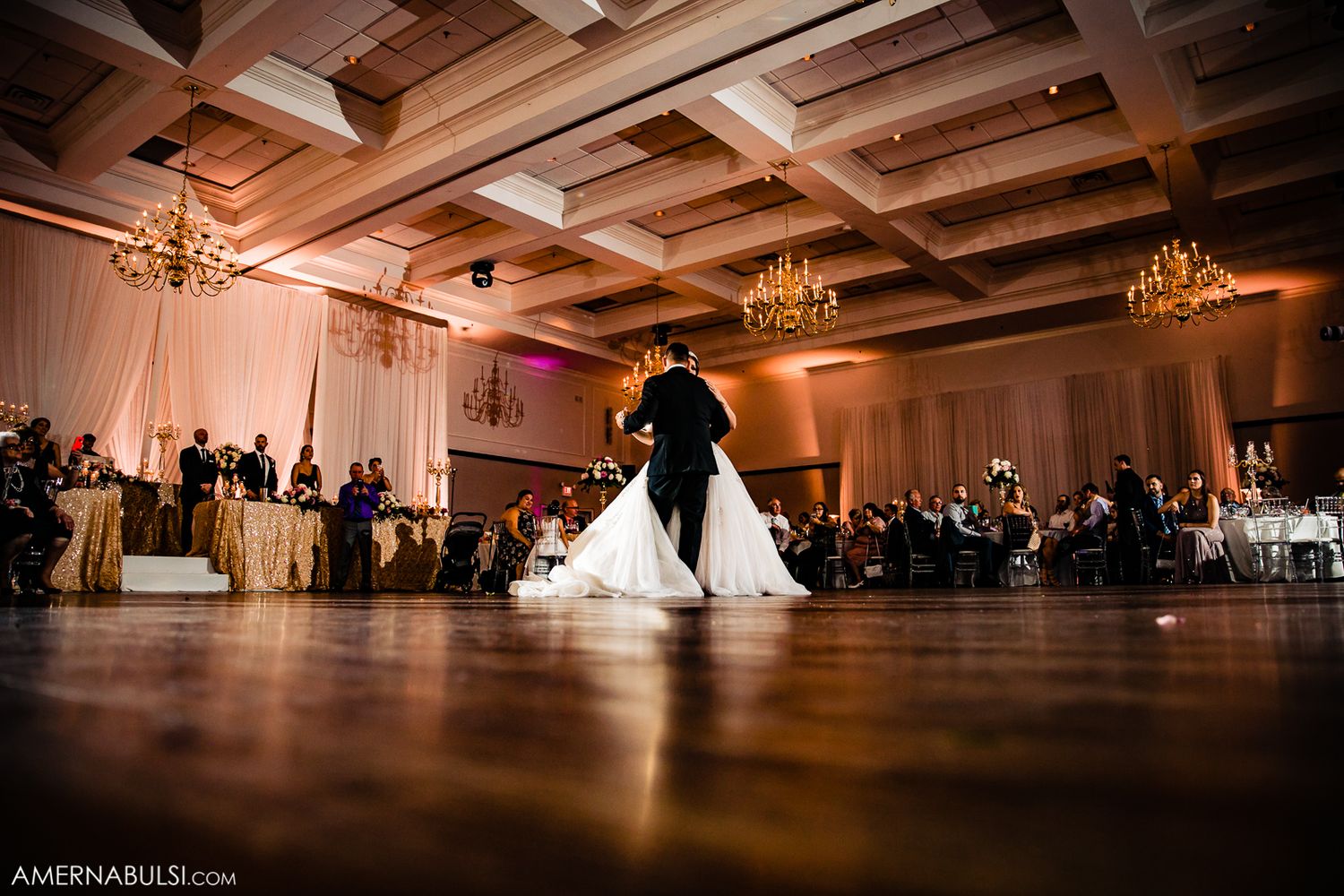 Panoramic view of an elegant ballroom with coffered ceiling and chandeliers set for a wedding reception.