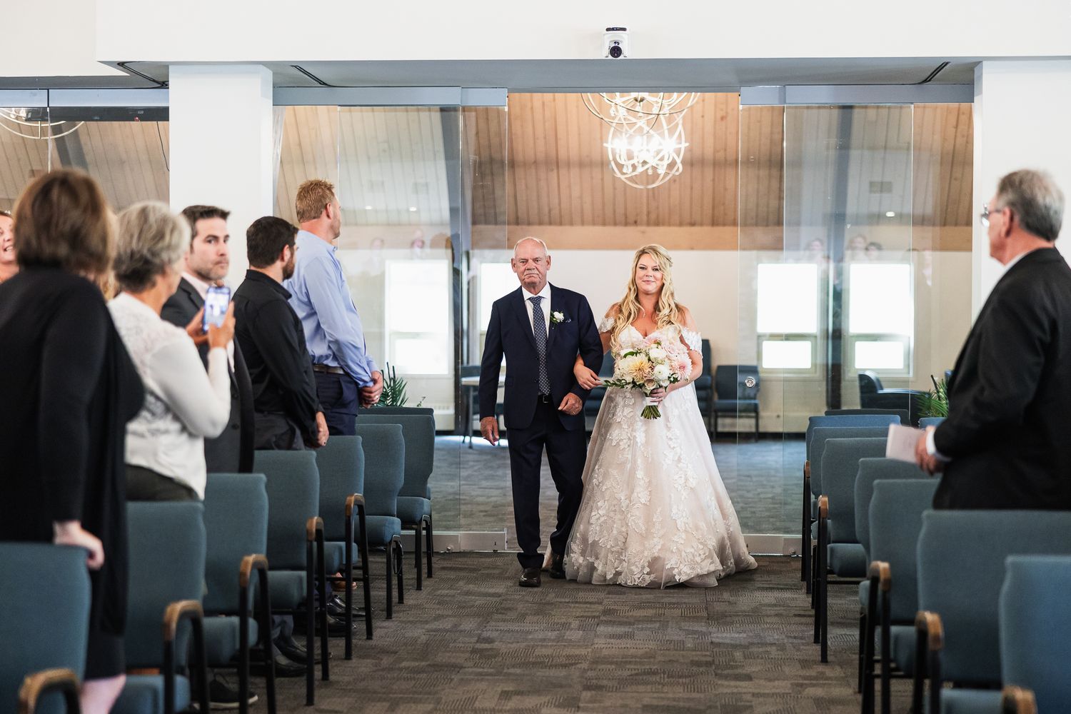 Intimate indoor wedding ceremony with elegant blue chairs and a chandelier hanging from the ceiling.