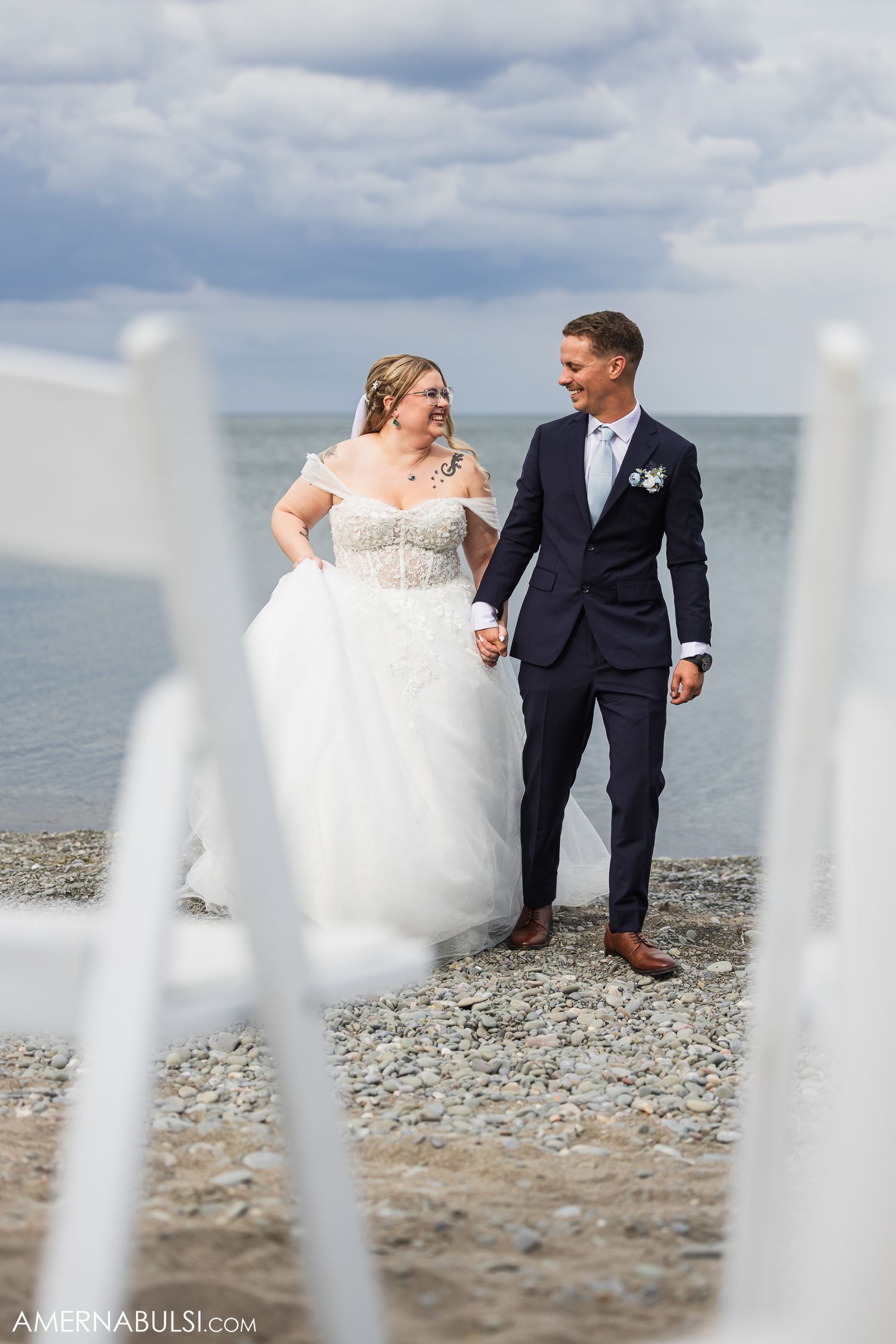 Newly married couple poses together on a rocky beach against cloudy skies.