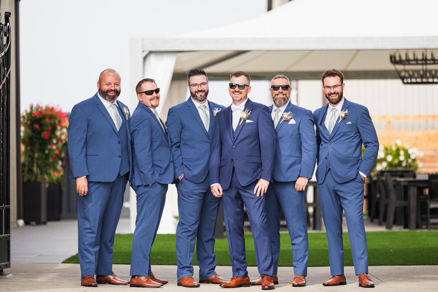Groomsmen in matching blue suits pose together outdoors at wedding venue.