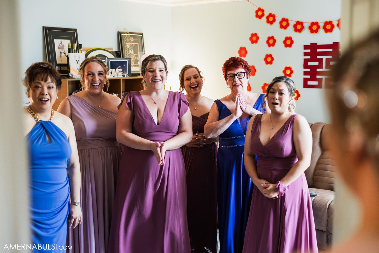 Bridesmaids in varying shades of purple and blue dresses smile together.