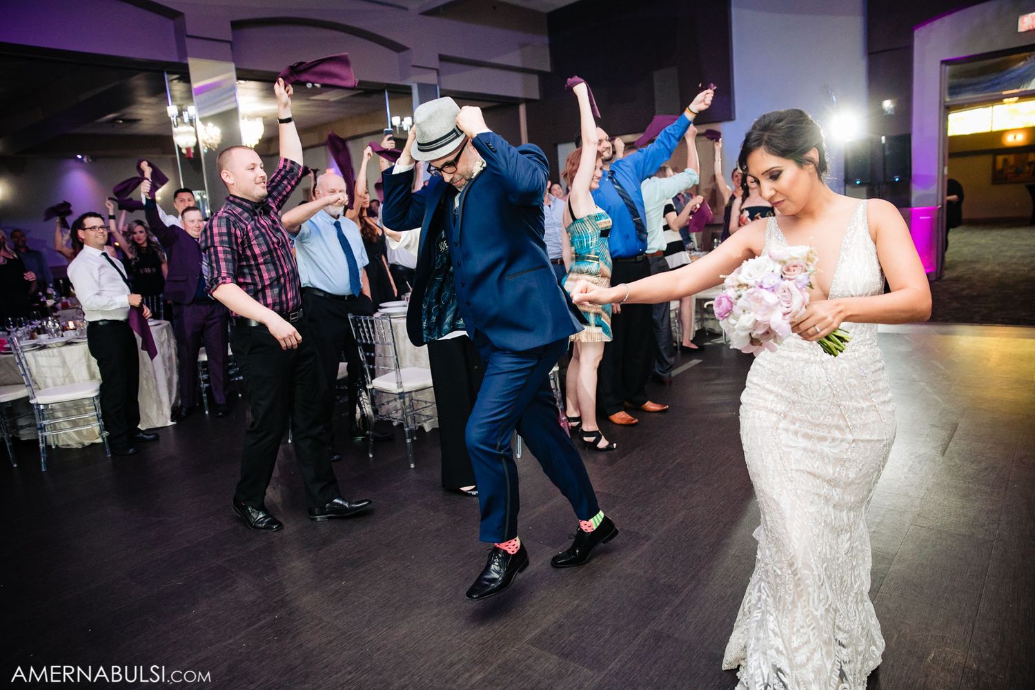Wedding guests dancing energetically on a dimly lit dance floor during reception celebrations.