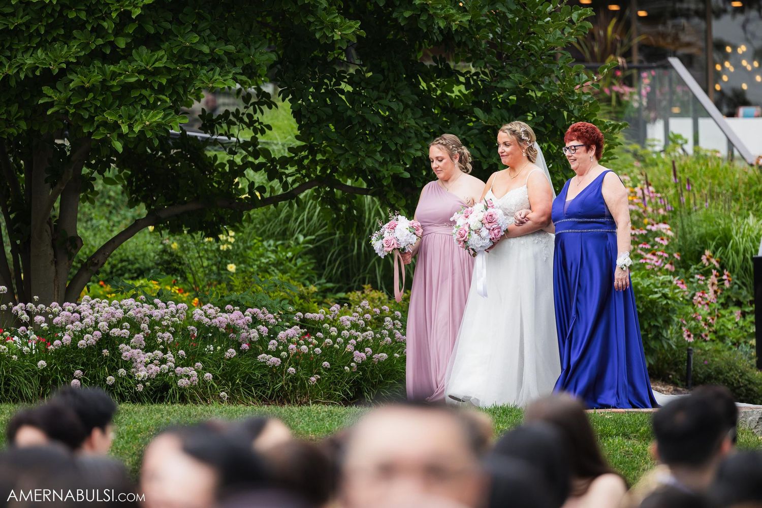 Wedding party stands against a garden backdrop with floral decor during an outdoor ceremony.