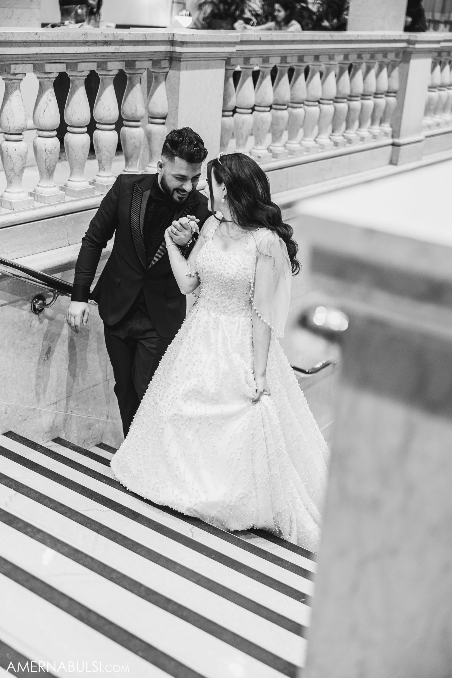 A couple in wedding attire dances gracefully on a white stone balcony with elegant balustrades.