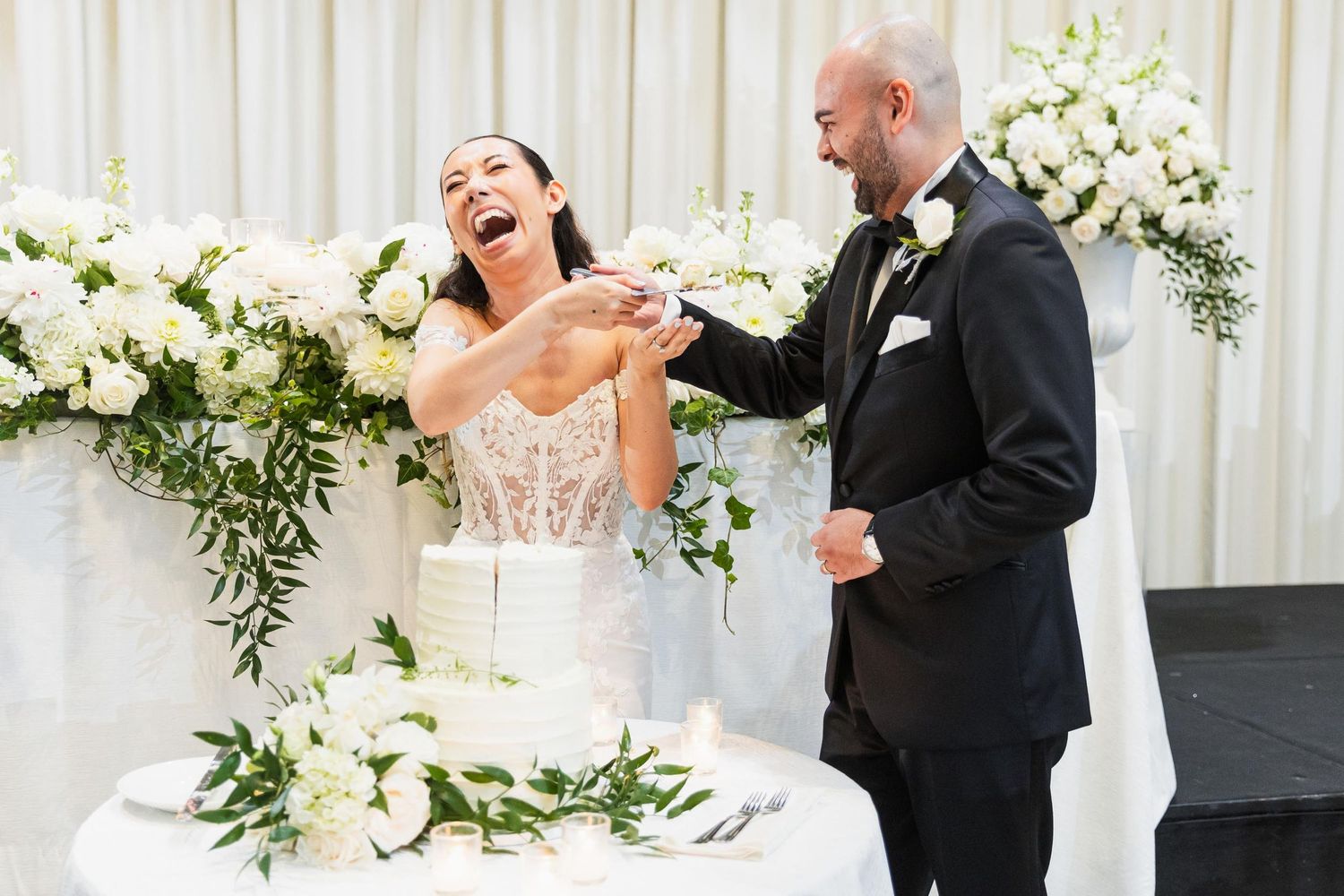 Couple shares joyful laughter while cutting their wedding cake.