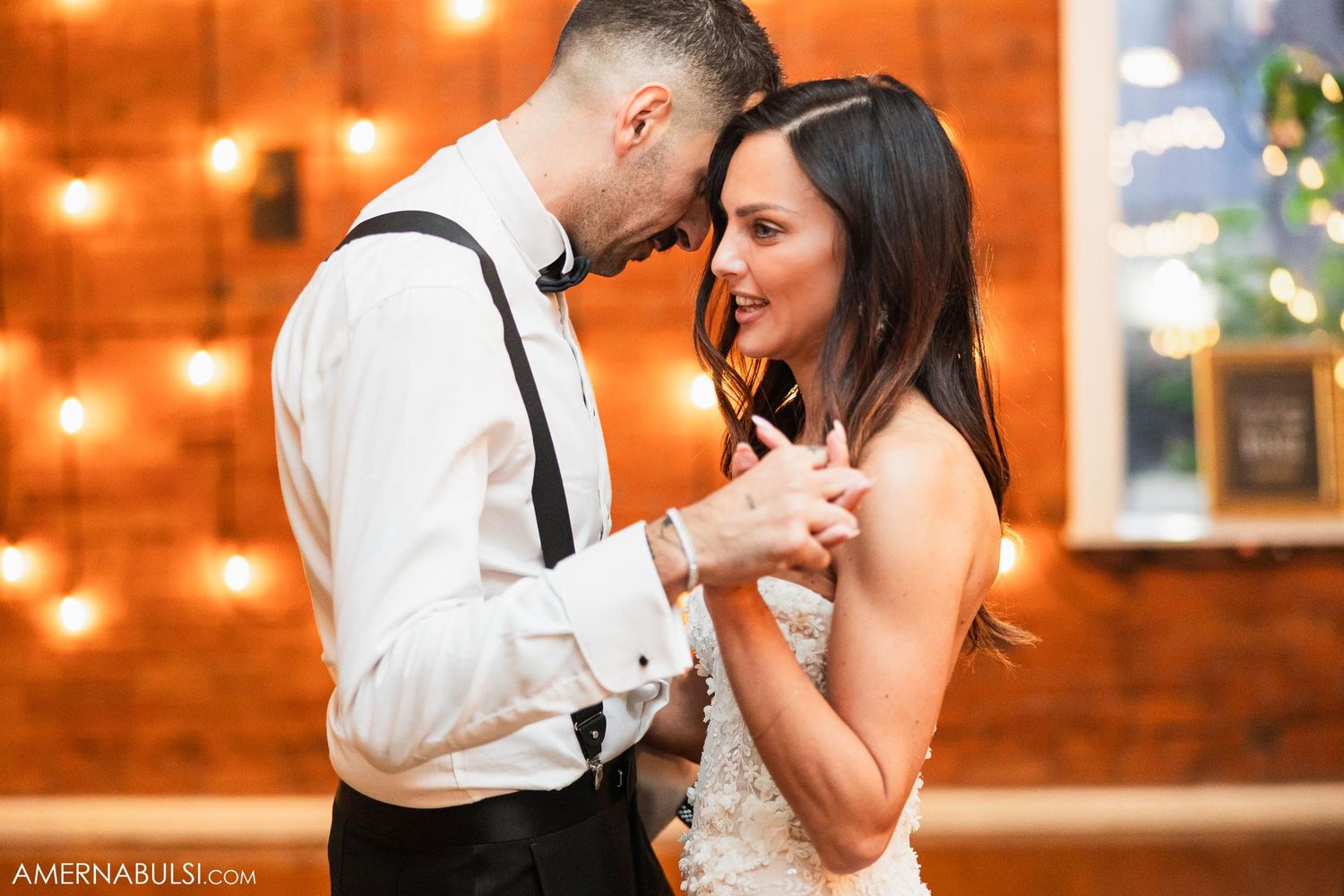 Intimate dance moment beneath warm string lights against exposed brick wall.